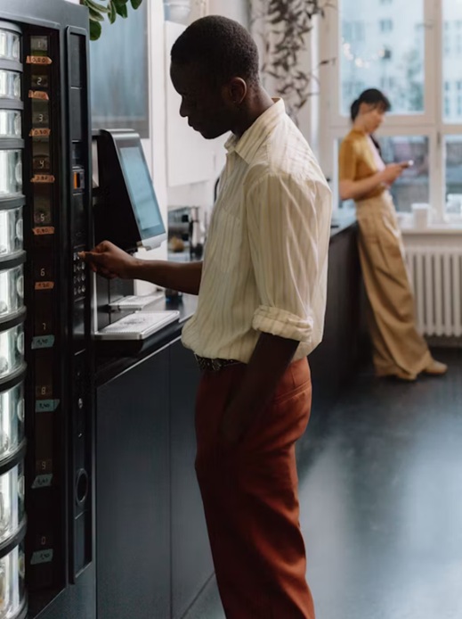 Person using office vending machine with coworker in background